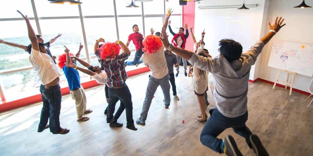 Ladies and gentleman team building, jumping in an empty office, some wear wigs