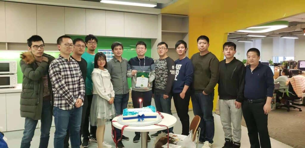 Ladies and gentleman celebrating awards winning with a cake and a man holding a plaque in the office