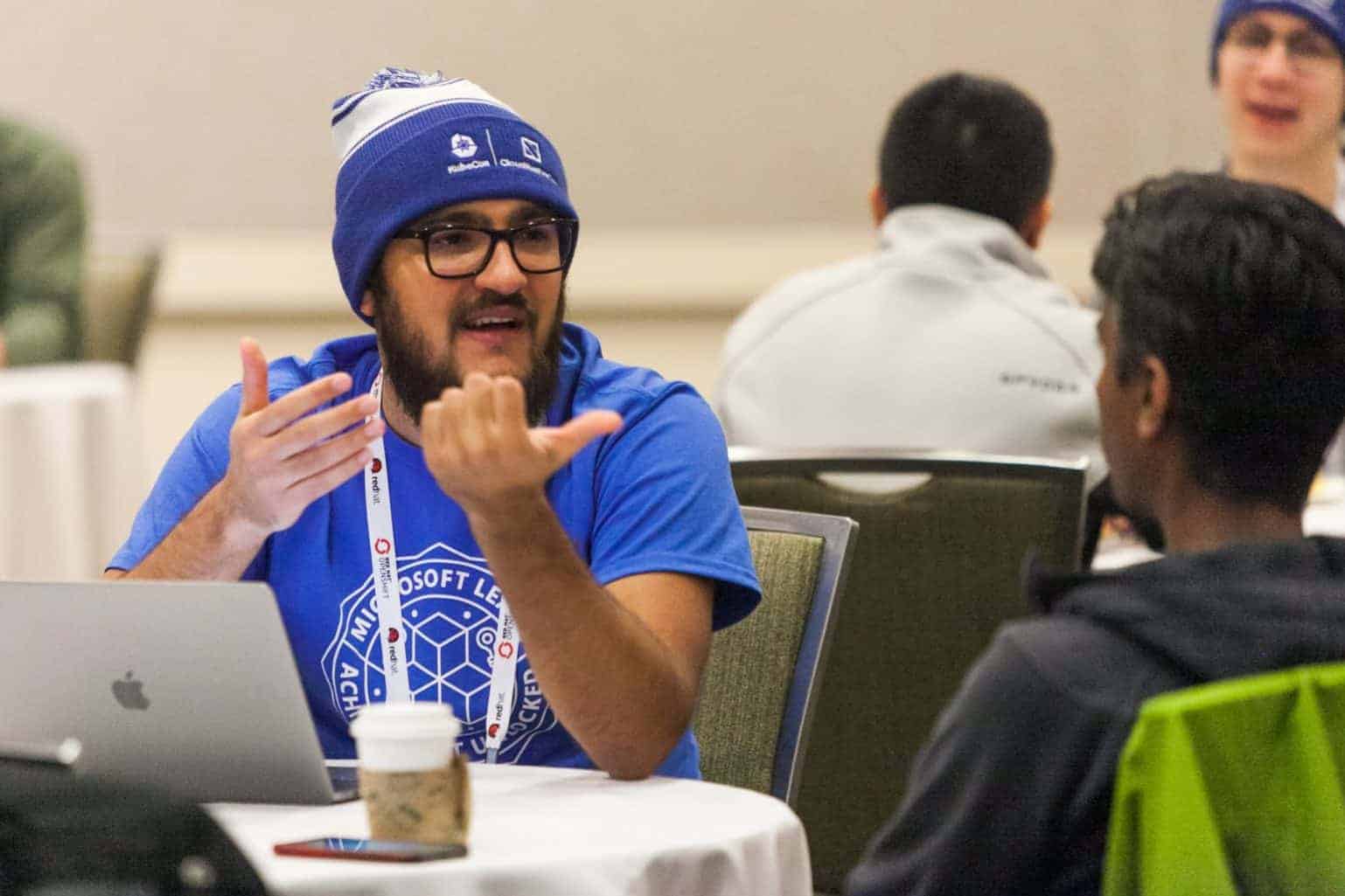 Dennis Salamanca Farafonov wearing KubeCon + CloudNativeCon beanie hat in conversation with another gentleman