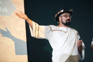 Baruch speaks on a stage wearing white costume