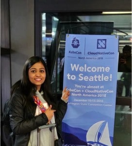 Surbhi Aggarwal in front of KubeCon + CloudNativeCon Welcome to Seattle banner
