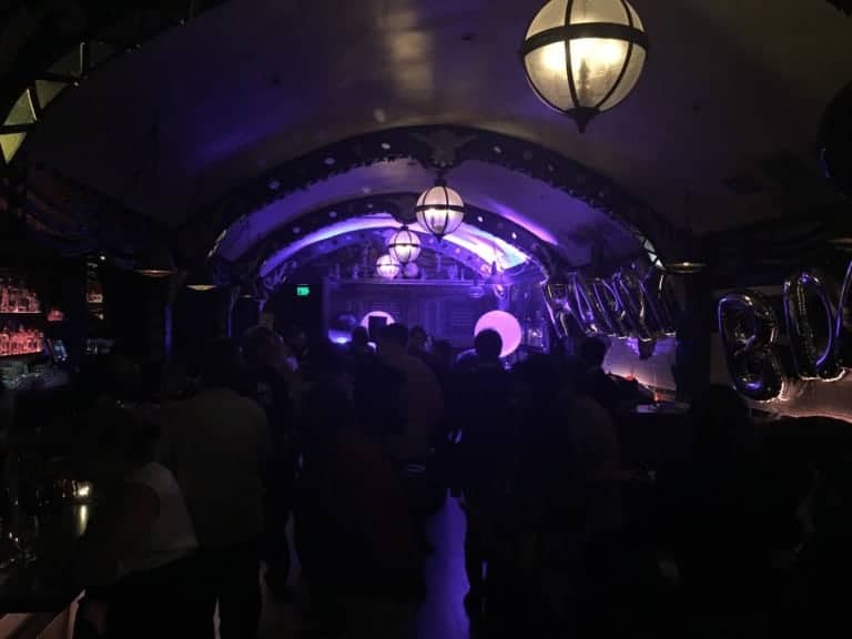 People hanging out in a bar with purple dim lights and Happy Bday balloon decoration