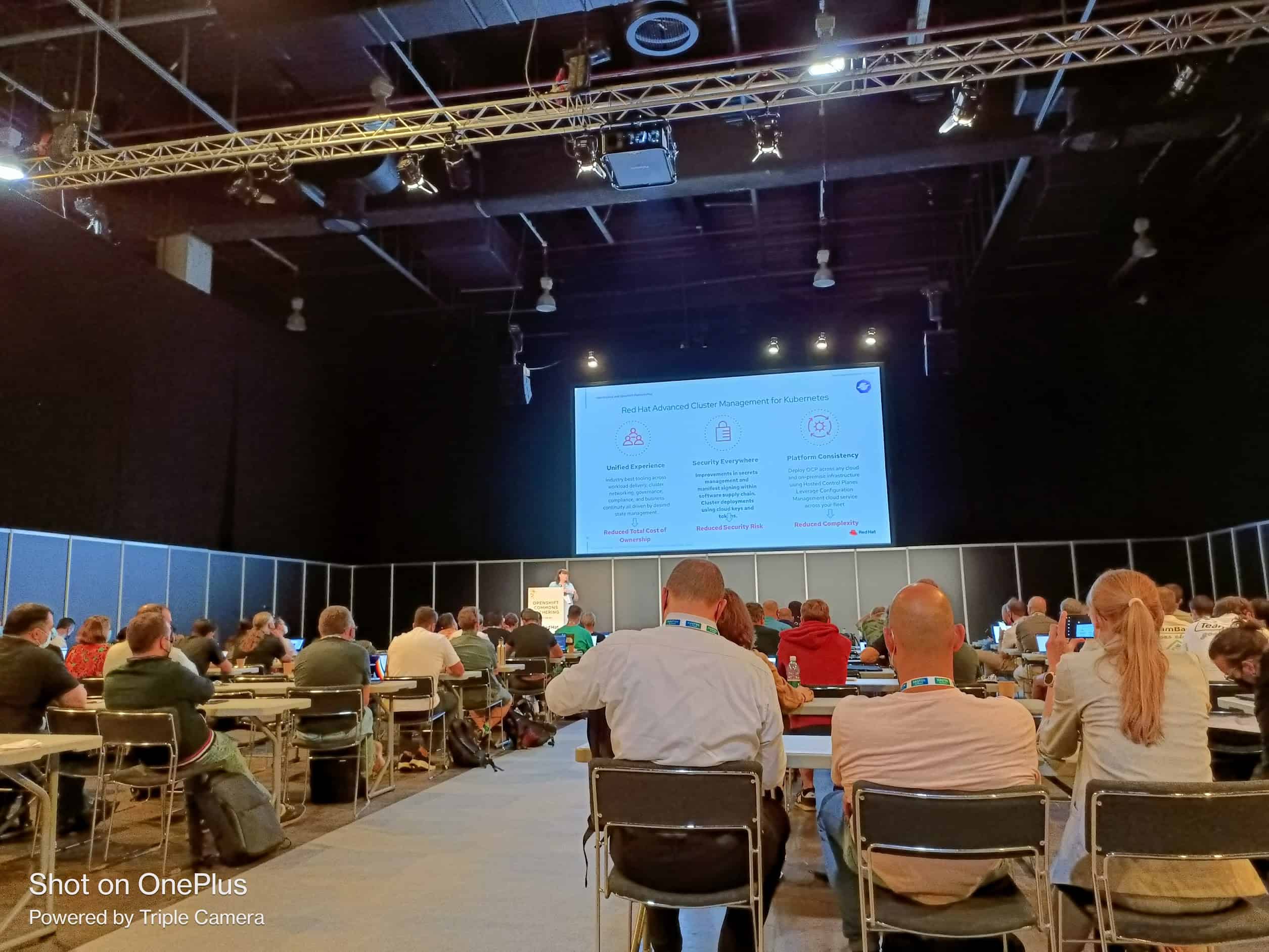 A lady presenting in front of audiences about Red Hat Advanced Cluster Management for Kubernetes in the hall