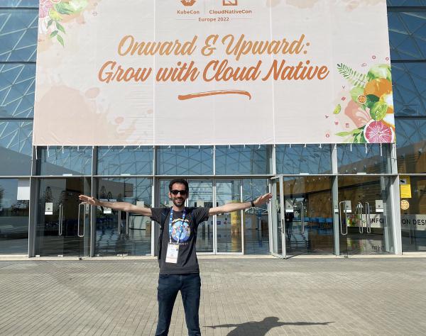 Stefan Prodan posing for picture in front of KubeCon + CloudNativeCon Europe 2022 conference hall entrance