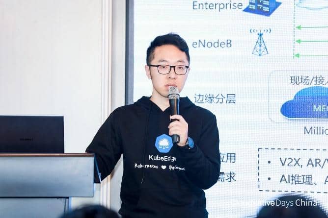 Kevin Wang wearing KubeEdge sweatshirt holding a mic presenting in front of participants