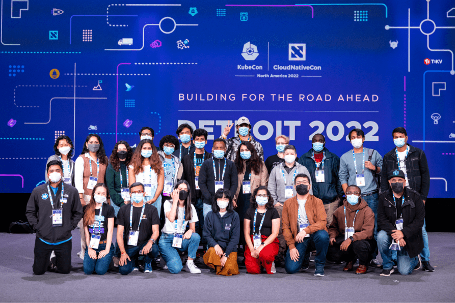 Ladies and gentlemen in masks have their picture taken in front of KubeCon + CloudNativeCon NorthAmerica 2022 event BANNER