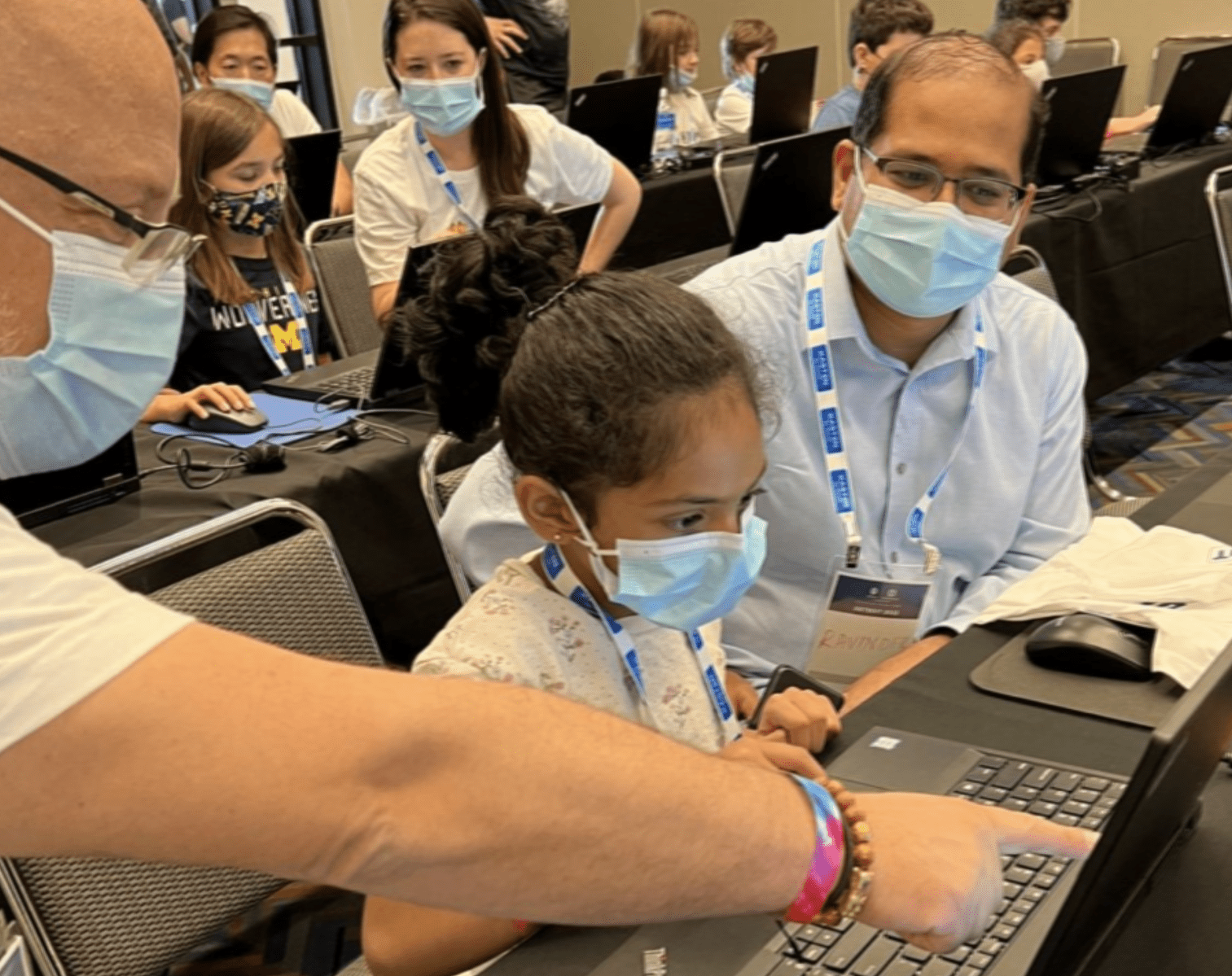 Girl on laptop guided by two mentors, one of the gentleman is pointing the laptop for the girl