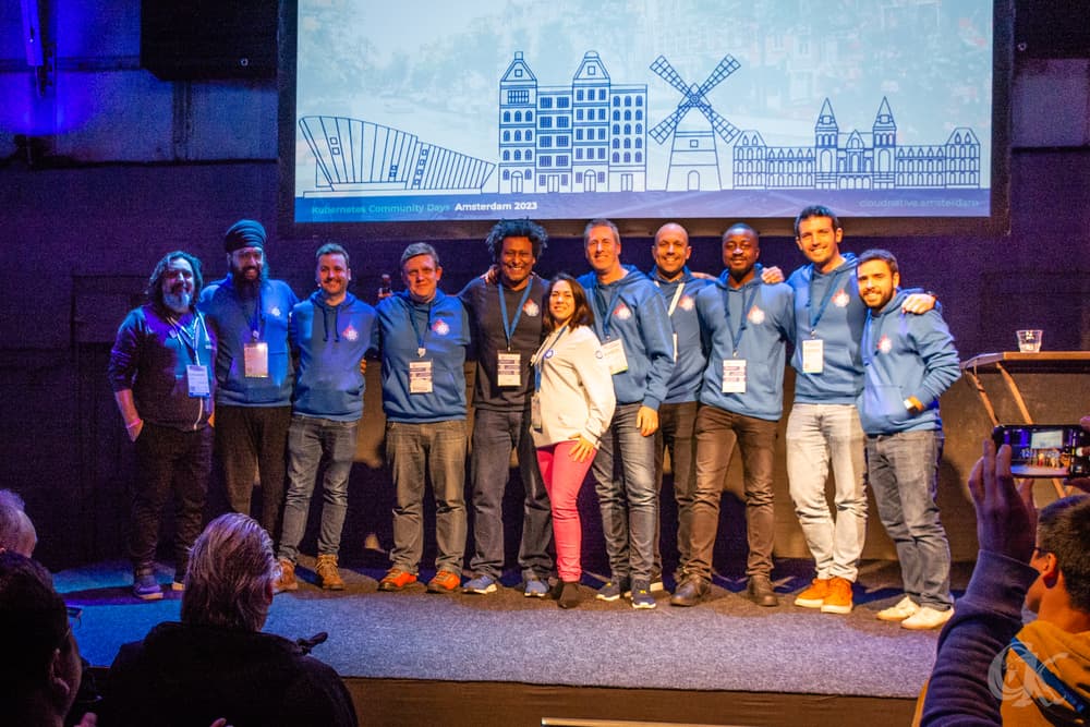 Lady and gentlemen having their picture taken on the stage in Kubernetes Community Days Amsterdam 2023 event
