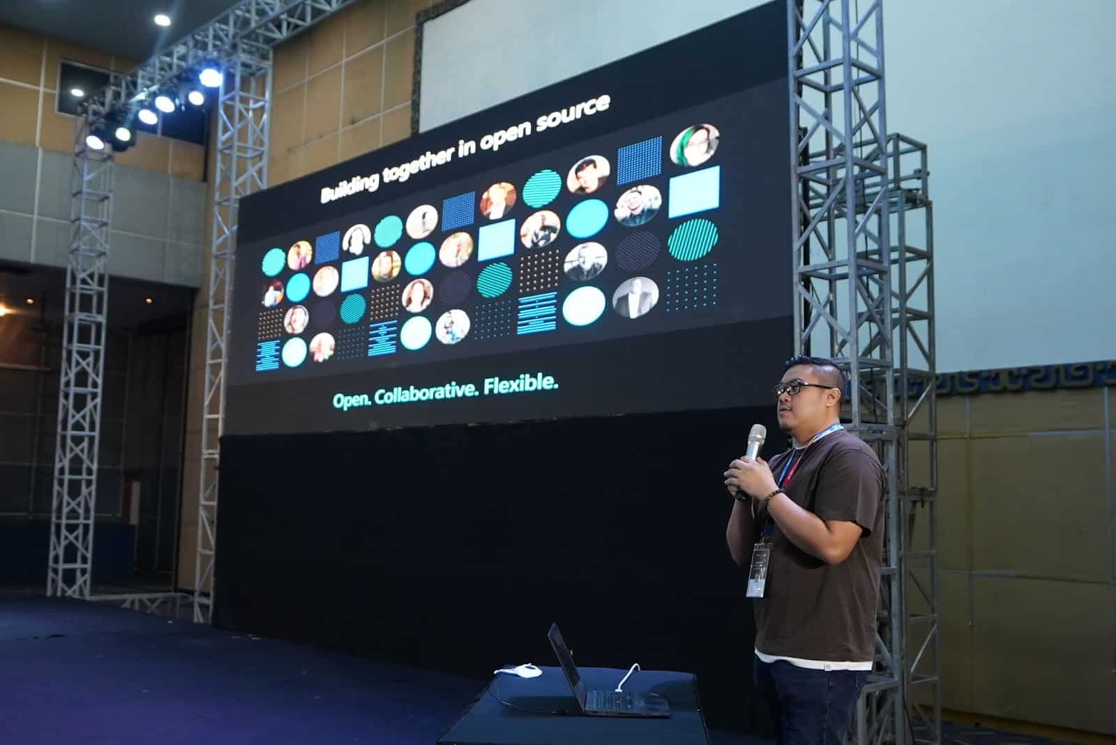 A gentleman in glasses holding a mic, presenting Building together in open source on the stage