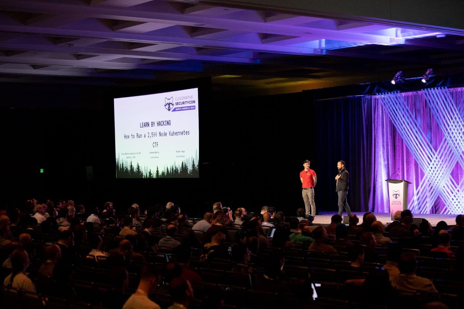 Two gentlemen doing presentation regarding Learn by Hacking - CloudNative SecurityCon in the hall