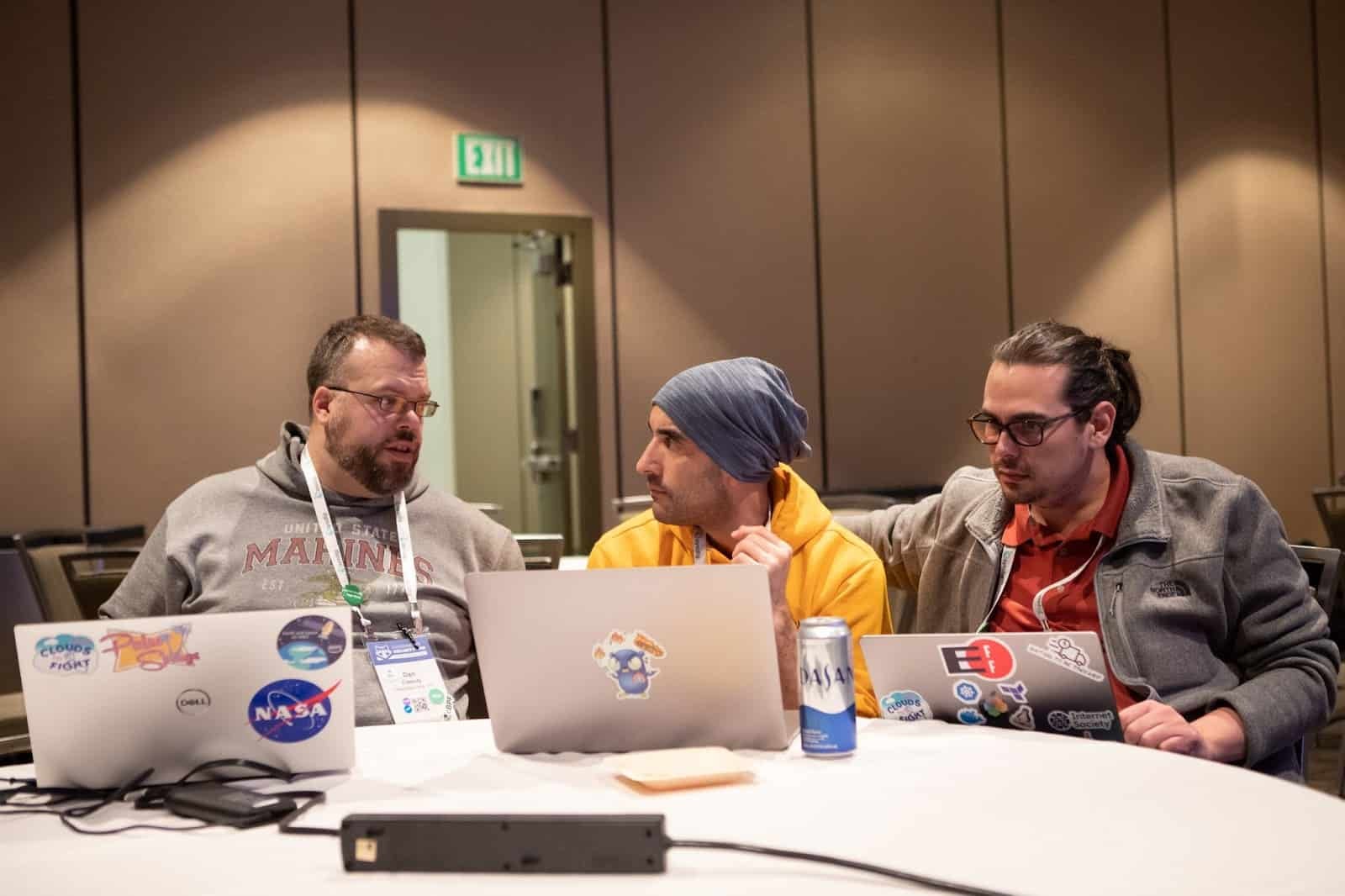 Three gentlemen in discussion on round table with their computers