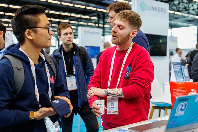 One gentlemen holding coffee making conversation with gentlemen in glasses in the event hall