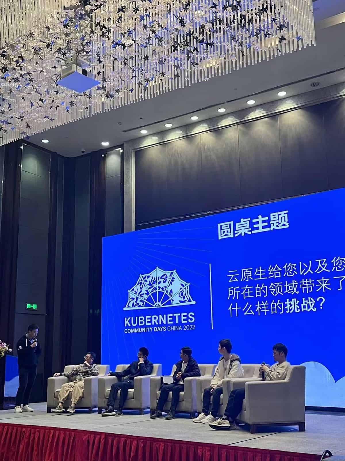 Gentlemen as speakers sitting on the stage of Kubernetes Community Days China 2022 lead by moderator
