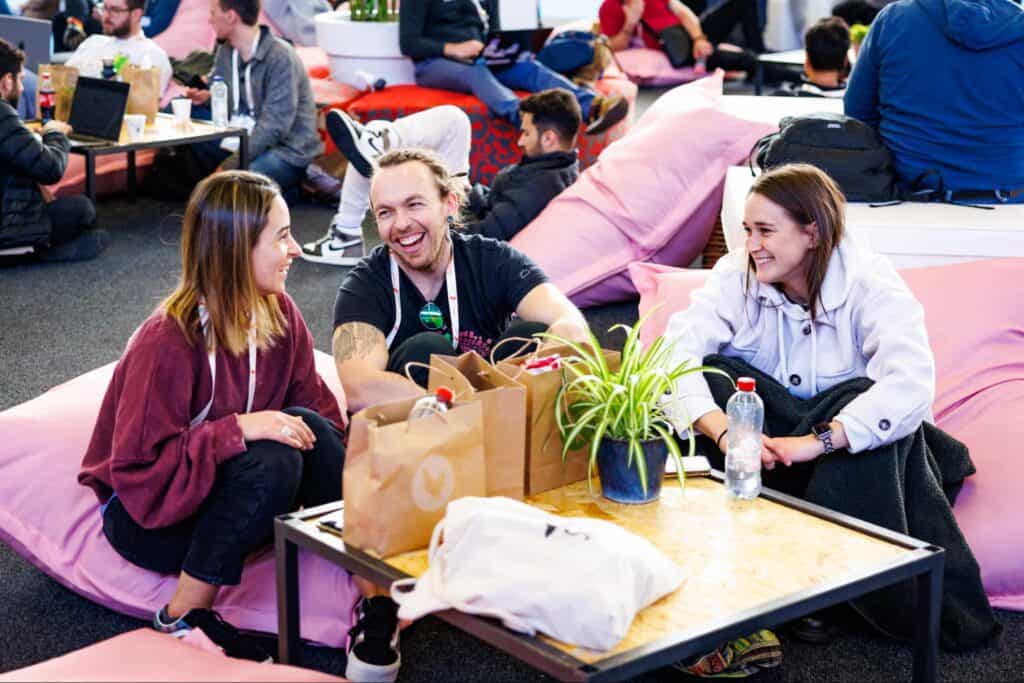 Two ladies and one gentleman sitting on beanbag and enjoying the conversation at KubeCon