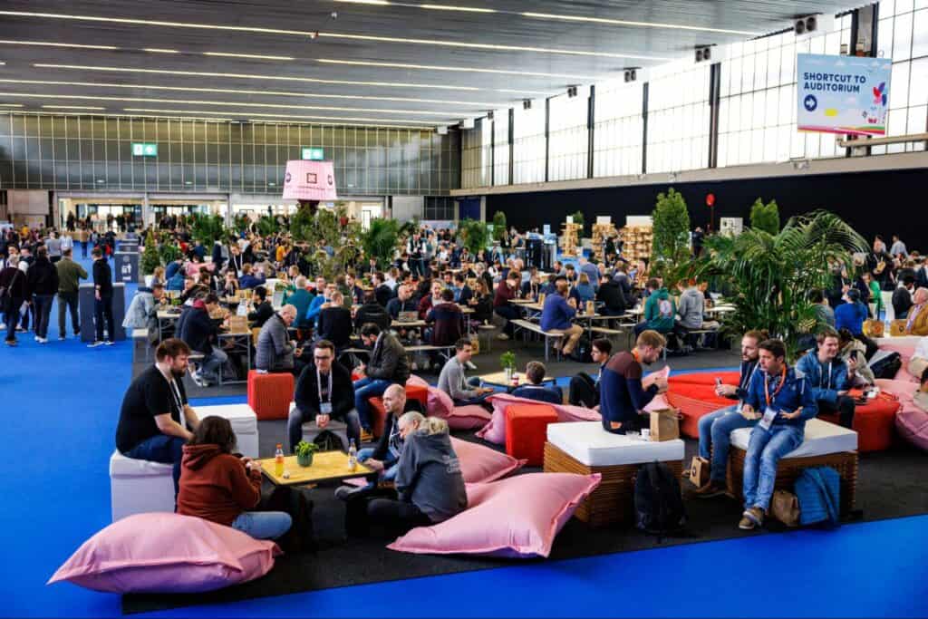 Participants sit in the beanbag and some are standing in conference hall at KubeCon