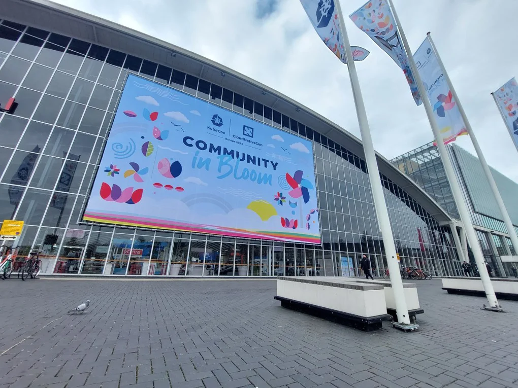 RAI Convention Centre with KubeCon event "Community in Bloom" banner and KubeCon flags in front of building