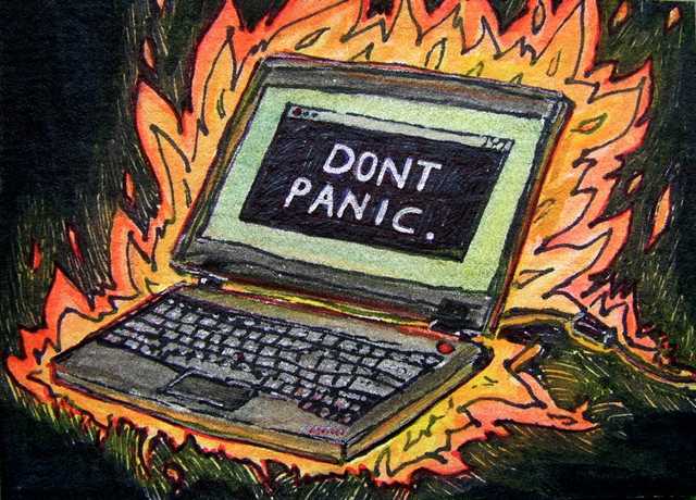 Burning laptop with "Don't Panic" words on screen