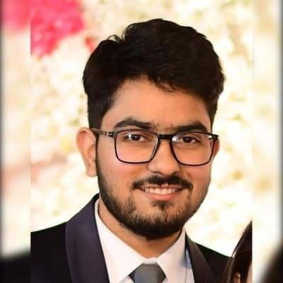 Mentee Ashish Dalal, wearing a suit, white shirt and grey tie, smiling into the camera. He is wearing glasses. There is a blurred 'bokeh' backdrop. 