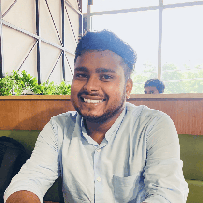 A photo of Mentee Abhishek Kumar. Abhishek is smiling, sitting in in a wooden booth/table with a window behind him. 