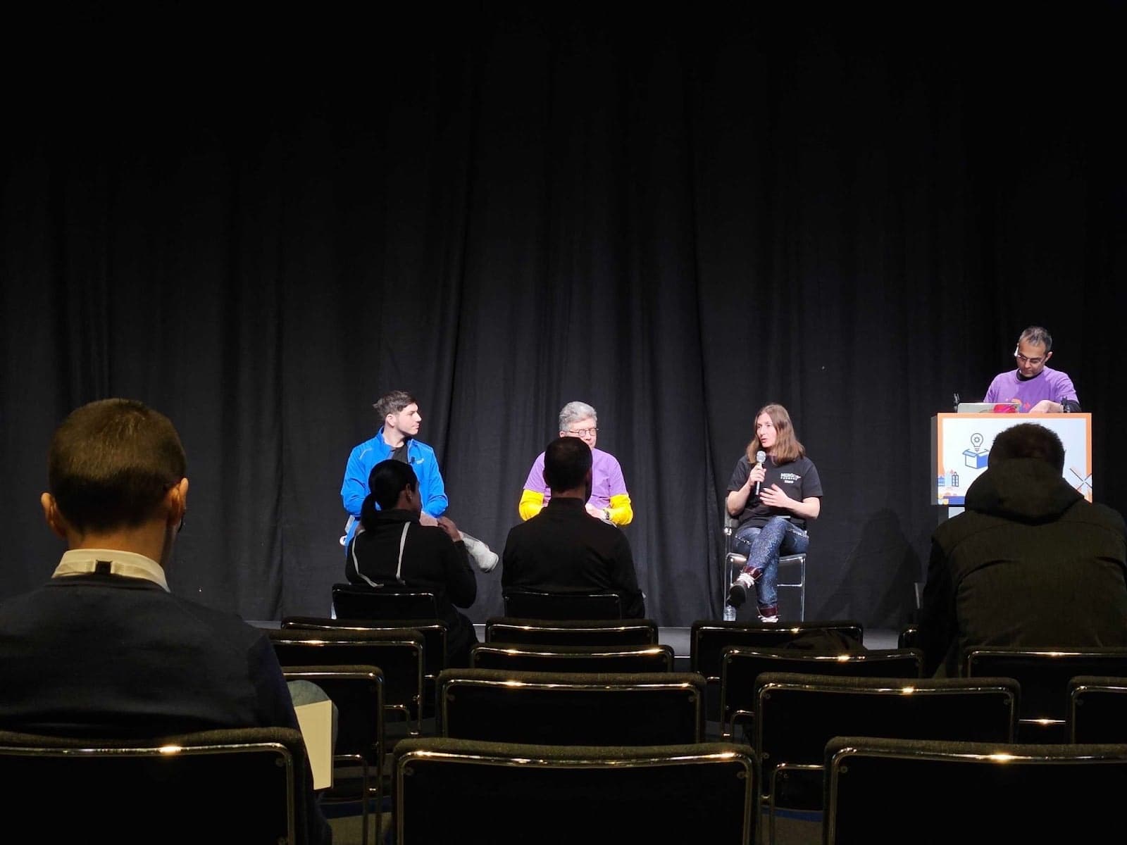 A photo of a Merge Forward panel discussion featuring three speakers and one moderator