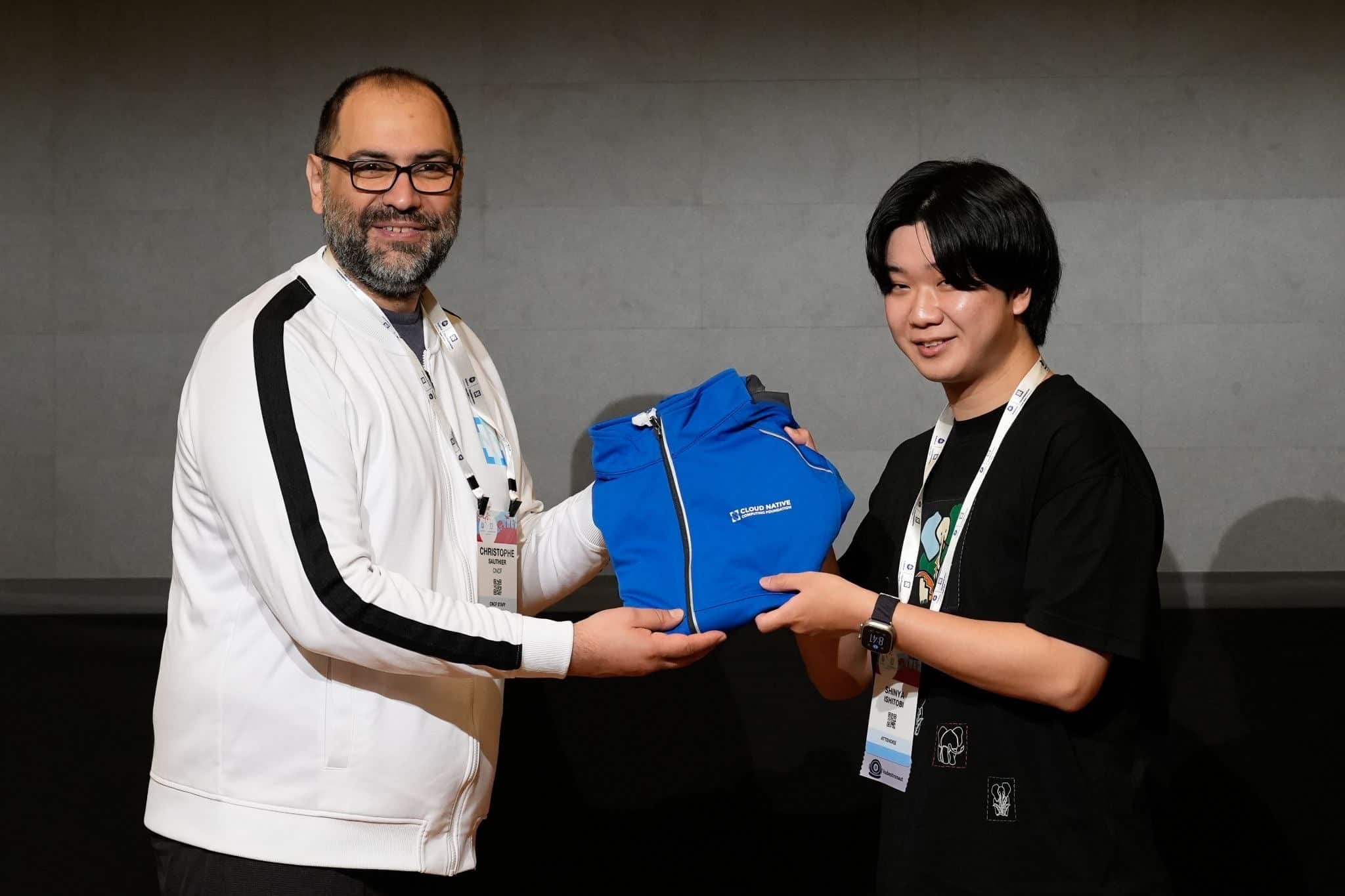 Christophe Sautier handing a blue Kubestronaut jacket to a new member of the crew